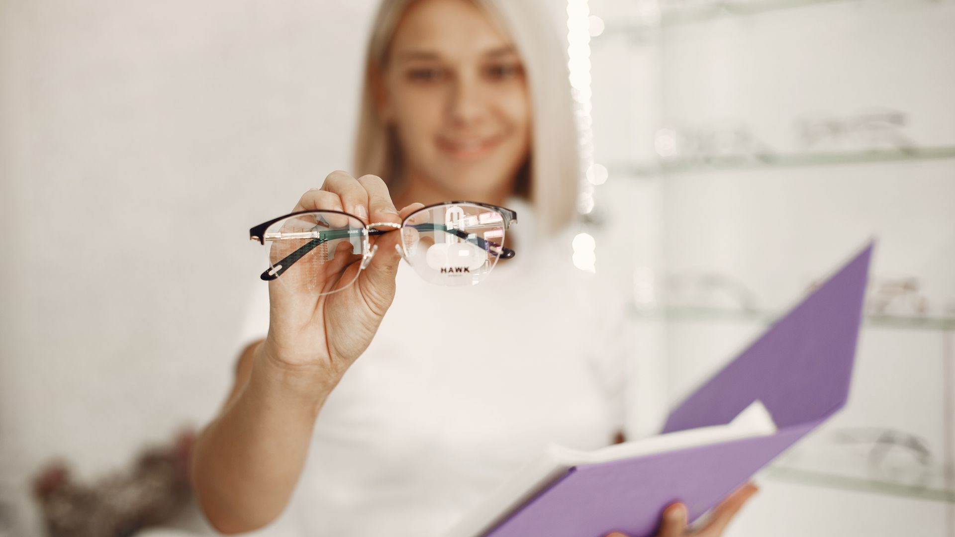 Augenoptikerin hält eine Brille in der Hand, im Hintergrund Brillenregale im Geschäft
